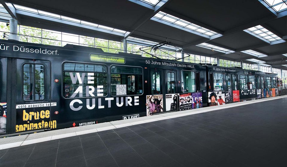 Bahn mit dem „WE ARE CULTURE“ Schriftzug. Neben dem Schriftzug sind mehrere Poster aus 50 Jahren Live-Entertainment zu sehen. 