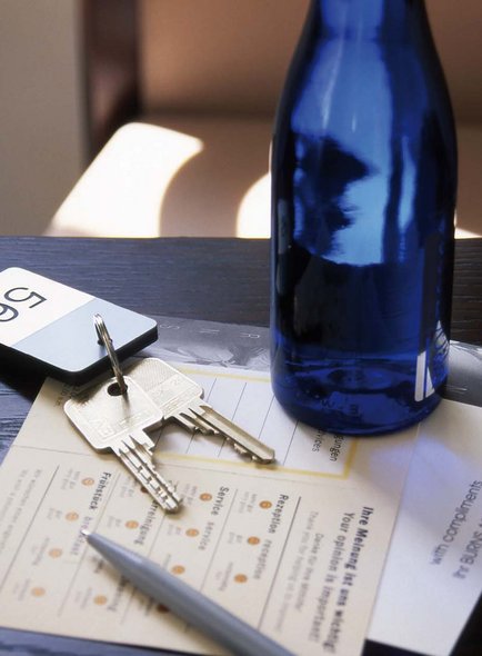 Zimmerschlüssel mit einer Flasche Wasser und Fragebögen auf einem Tisch. 